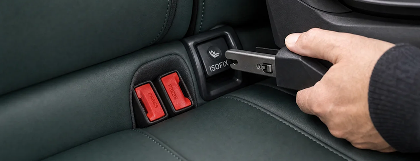 Isofix-fäste i baksätet där en hand fäster ett bilbarnstolsfäste i det röda ISOFIX-uttaget.
