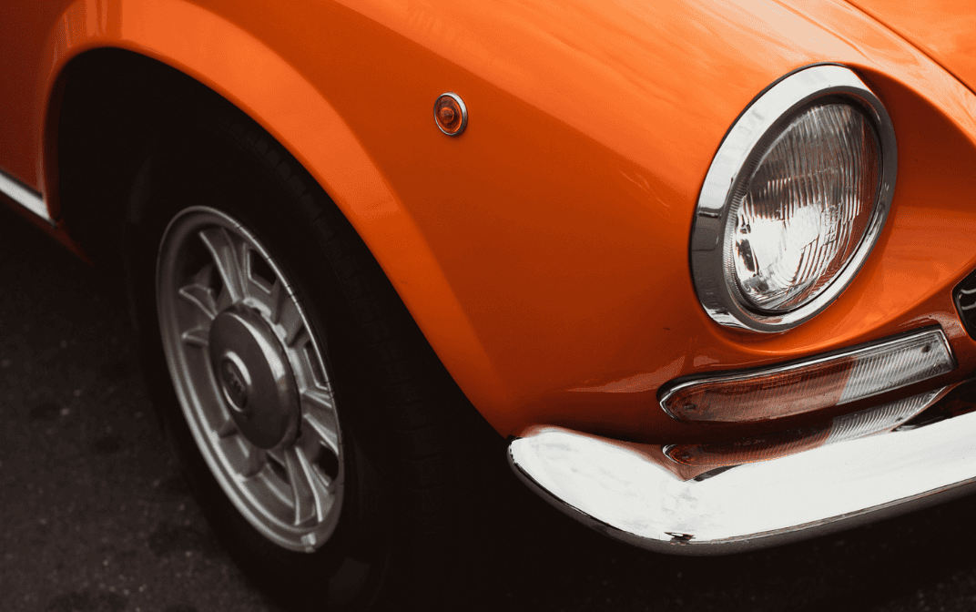 Närbild av en orange bil med strålkastare och framhjul.